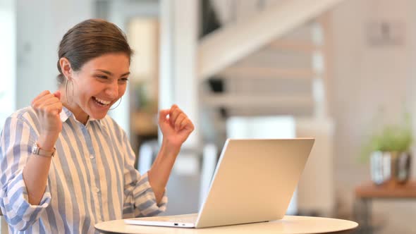 Excited Young Indian Woman Celebrating Success on Laptop in Cafe 