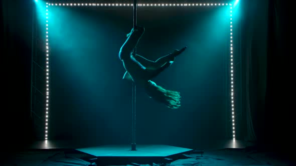 Slender Woman Performs Acrobatic Exercises on a Pole. Silhouettes in Soft Turquoise Light