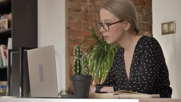 woman with glasses working on her laptop in her home office