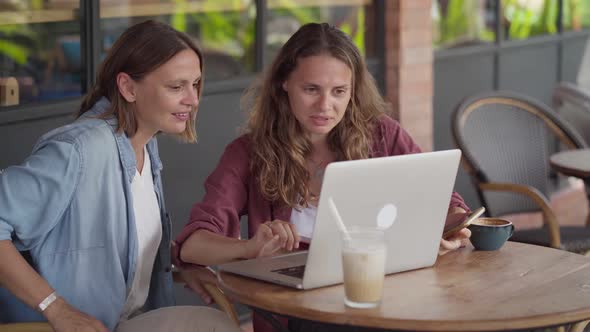 Happy Women Working Together with Laptop at Outdoor Cafe