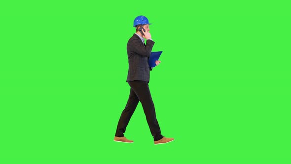 Millennial Businessman in Hardhat Talk on Smart Phone Call Walking Hold Clipboard with Documents on