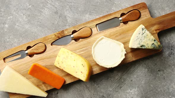 Assortment of Various Kinds of Cheeses Served on Wooden Board with Fork and Knives