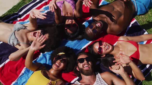 Diverse group of friends sunbathing together smiling and waving to camera