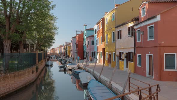 Waterside street with brightly painted houses and walking people Burano, Italy