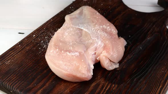 Hand Sprinkles Piece of Chicken Fillet with Salt and Spices are Sprinkling Before Preparation