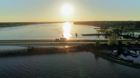 Cinematic Aerial View of Cars Driving on Bridge Across Lake at Summer Sunset