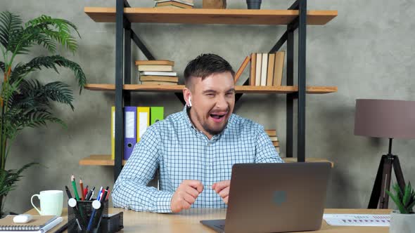 Yawning bearded businessman at home office sitting on chair at desk with laptop