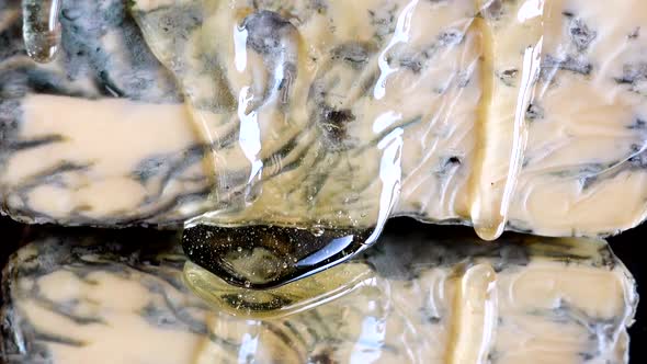 Drops of honey flowing down from the Dorblu cheese on a mirrored black background.