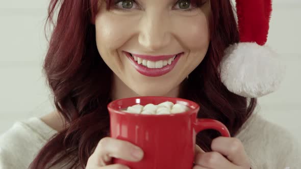 Woman raising mug of cocoa and marshmallows to face