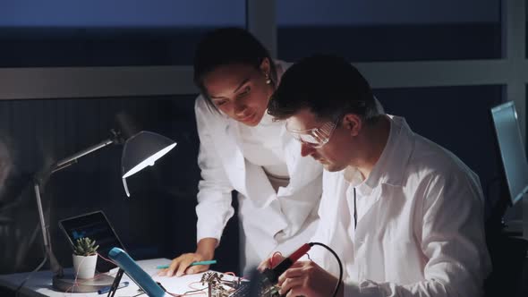 Two Mixed Race Electronics Engineers Working with Multimeter Tester and Other Electronic Devices