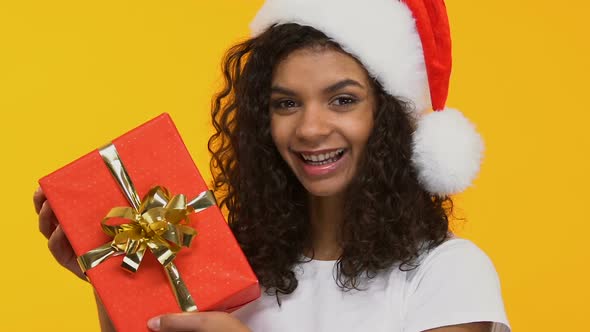 Beautiful Girl in Santa Hat Showing Present to Camera, Christmas Celebration