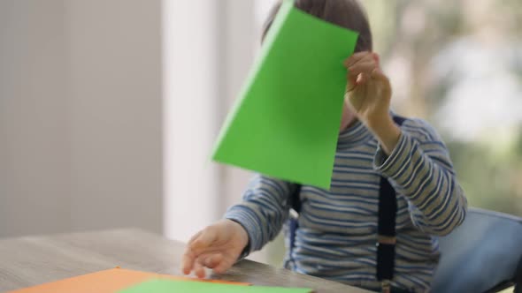 Curios Autistic Caucasian Boy Sitting at Table with Colorful Paper Smiling Looking Away