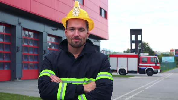 A Firefighter Looks at the Camera with Arms Folded Across Chest - a Truck Drives Into a Fire Station