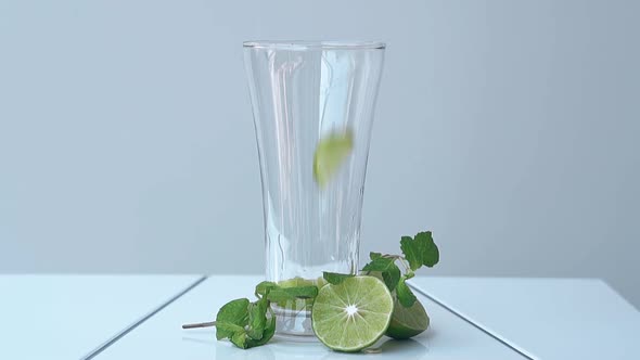 Mint Leaves Fall Into Tall Shining Glass Near Lime Halves