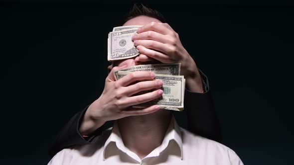 hands from dark tightly cover mouth with money to a young man in a white shirt