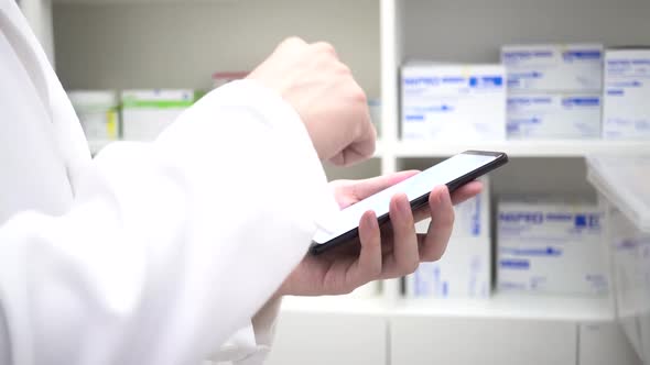 Pharmacist Using Mobile Phone at Drugstore Room