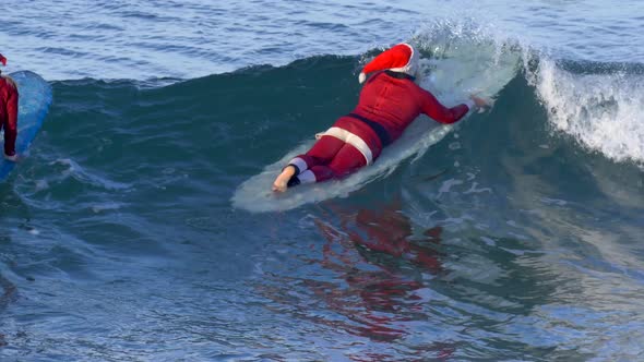 Santa Claus paddles out to go surfing.