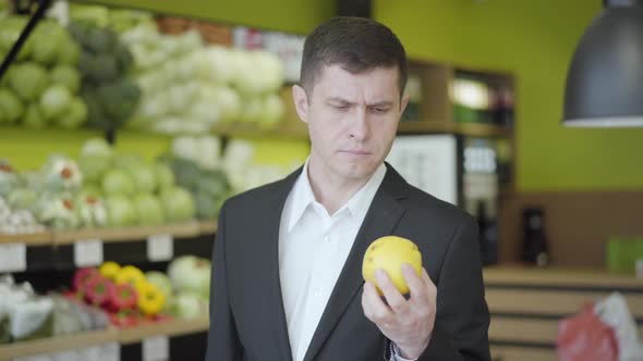 Portrait of Confident Serious Man Selecting Pear in Supermarket. Young Caucasian Guy Choosing Yellow
