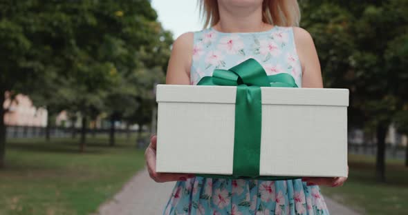 A Woman in a Summer Dress Carries a Gift in a Beautiful Box Walking Down the Street of the City
