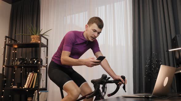 Man is typing messages on smartphone while training on stationary bicycle
