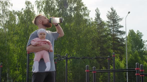 Athletic Caucasian Dad with Baby Daughter Drinking from Sports Bottle