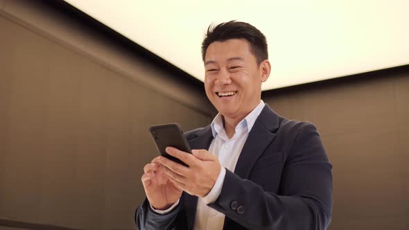 Confident Korean Man Using Mobile Phone App in Modern Light Office