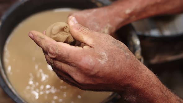 Hands Male Potter are Kneading Clay Against Background Container with Water Top View