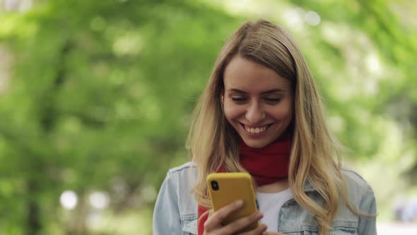 Young Woman Using Smartphone Walking Down the Park