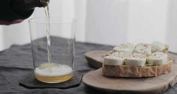 Slow Motion Pour Wheat Beer in a Tumbler Glass Next to Ciabatta Sandwiches with Mozzarella and Pesto