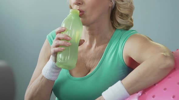 Aged Female Resting Elbow on Fitness Ball and Drinking Water After Exercising