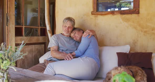 Smiling senior caucasian couple embracing and relaxing on porch with pet dog