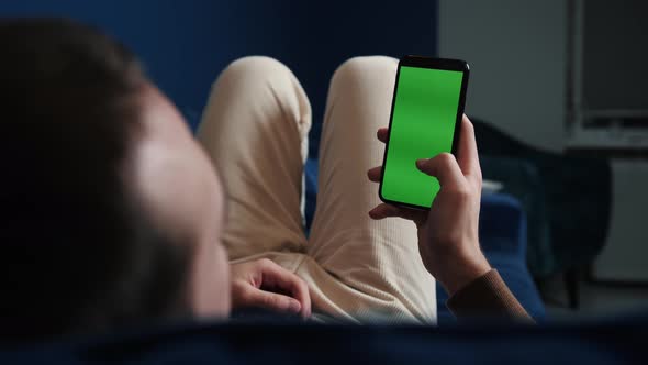 Man Lying on Couch Using Smart Phone with Chroma Key Green Screen at Night, Scrolling Through Social