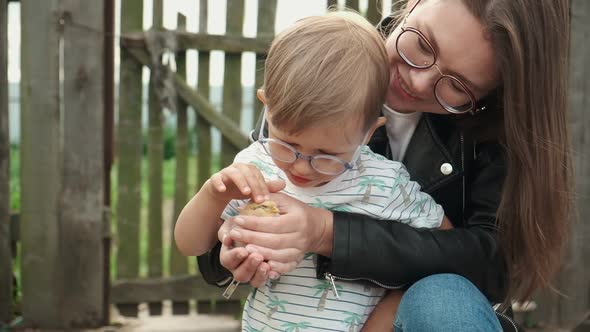 Child and Mother Holding a Chick in Hand in Backyard of Farm