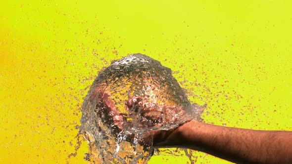 Blue Water Balloon Is Popping In A Hand On A Yellow Background In Slow Motion