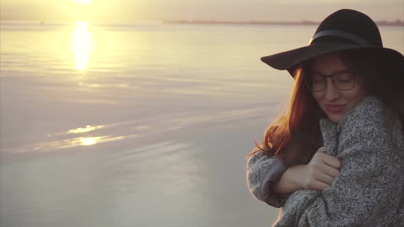 Young Pretty Woman in Black Hat and Glasses Near the Sea at Sunset