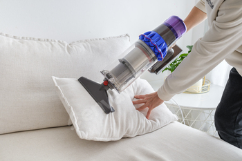 Person using handheld vacuum cleaner on sofa cushion