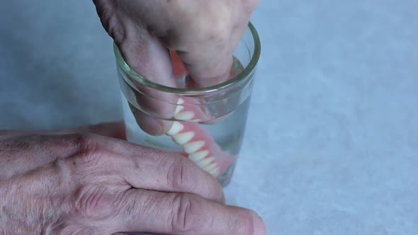  The pensioner removes dentures and puts them in a glass of water.