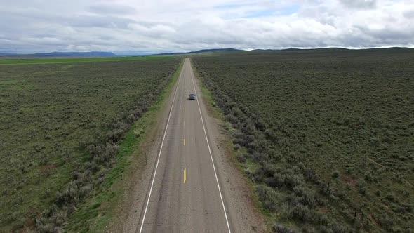 Drone following car on road in a vast landscape