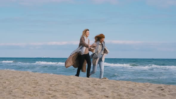 Woman Couple Run Holding Hands Along the Sea Beach