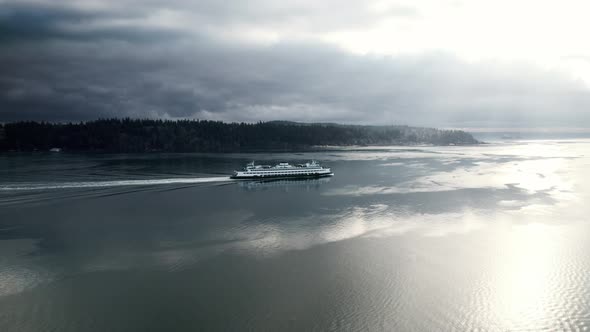 Commuter ferry cruises along dark water reflecting streaming sunlight and gloomy clouds, aerial
