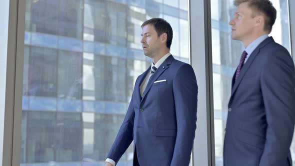 Two Middle Aged Businessmen Having Conversation and Pointing Outside the Window