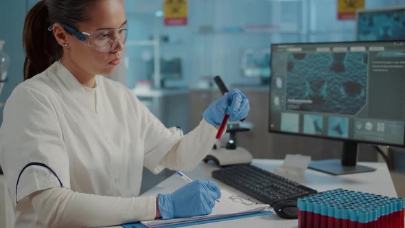 Woman Scientist Looking at Test Tube and Taking Notes