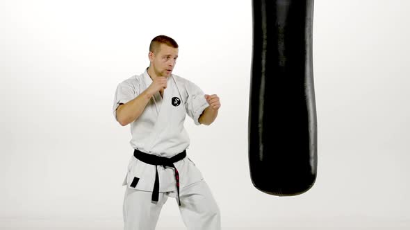 Black Belt Karate Man Practicing on the Sandbag on White Background