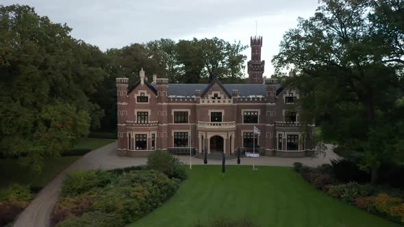 Drone quickly descending towards entrance of beautiful old mansion on green estate