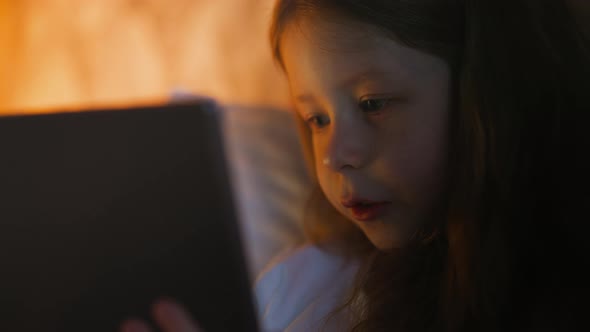 Little Child Talks at Video Call Via Tablet Lying in Bed