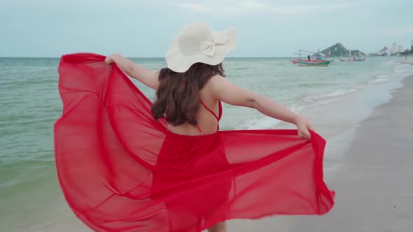 slow-motion of cheerful woman in red dress walking on the sea beach