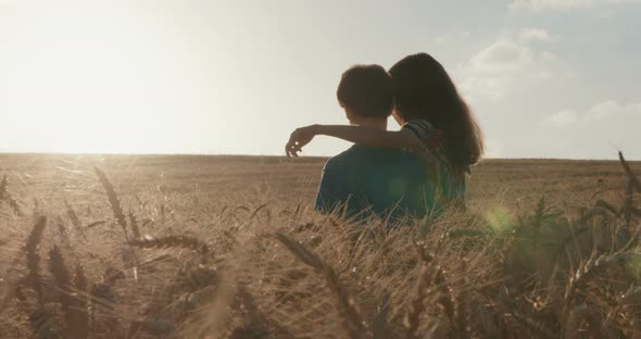 Boy and girl running in a golden wheat field together towards the sunset