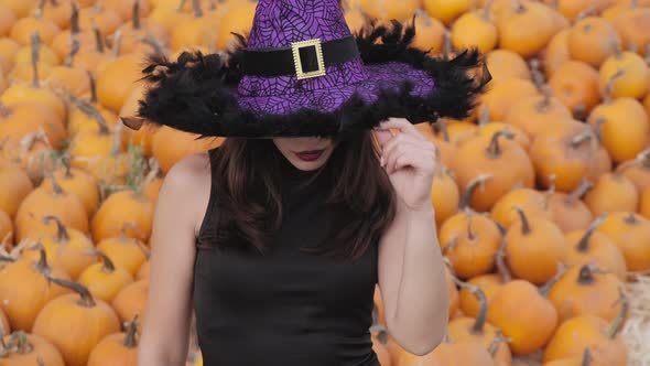 Beautiful girl in a black dress and a purple witch hat poses against the backdrop of a large number
