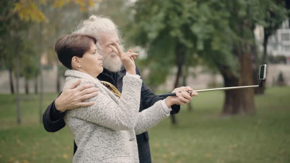 Side View of Modern Couple of Retirees Using Video Chat on Smartphone Outdoors