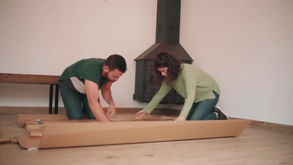 Man And Woman Unboxing Parts Of DIY Table On The Floor. wide